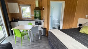 Una habitación compacta y moderna con cama, una mesa de comedor con sillas, una pequeña kitchenette y zona de ducha.