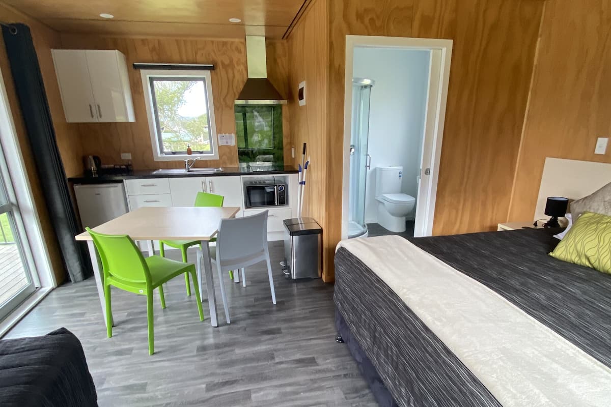 Une chambre compacte et moderne, comprenant un lit, une table à manger avec des chaises, une petite kitchenette et un espace douche.