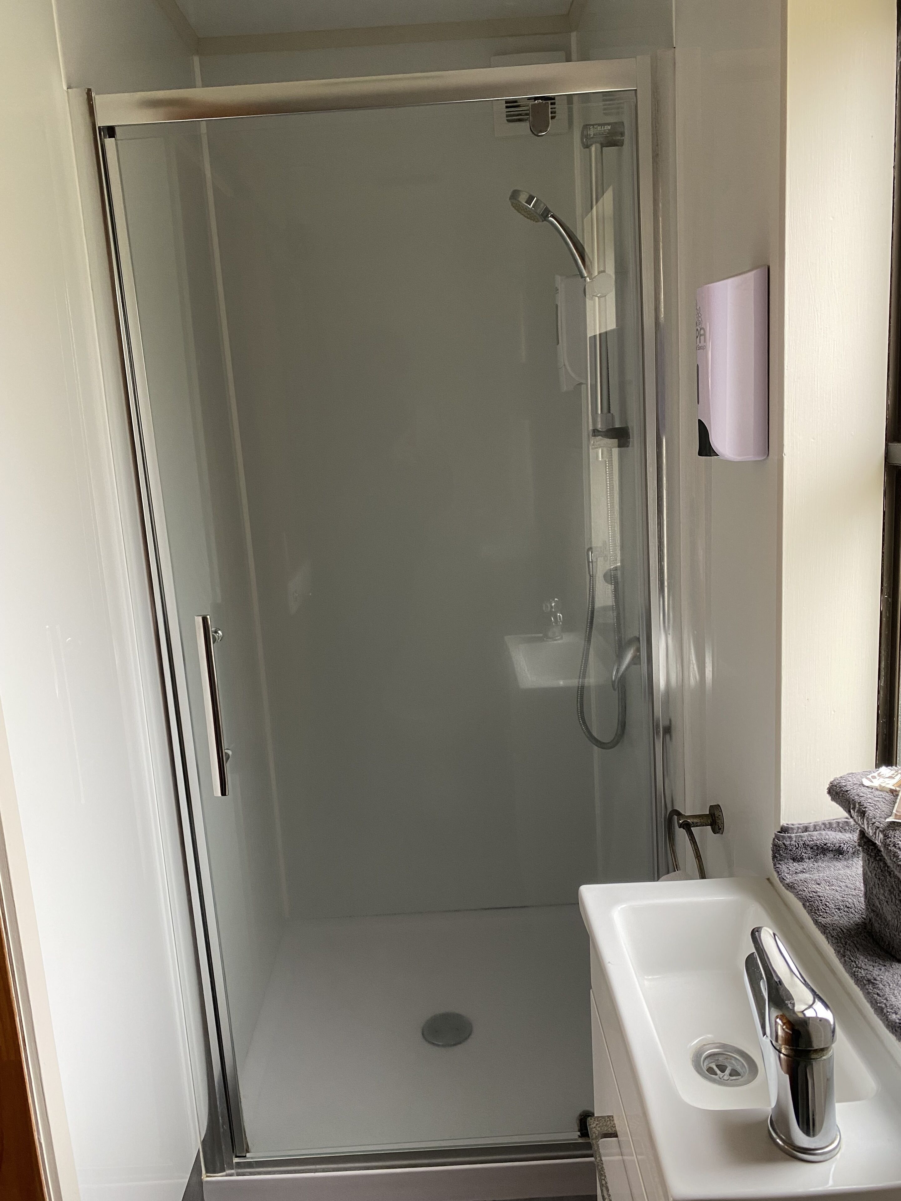 A modern bathroom with a glass-enclosed shower, a white sink, and a towel rack.