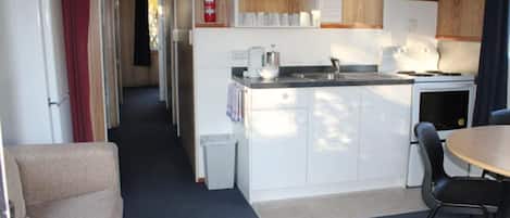 A compact kitchen with white cabinets, a small countertop, and a sink. There is a dining area with a table and chairs.