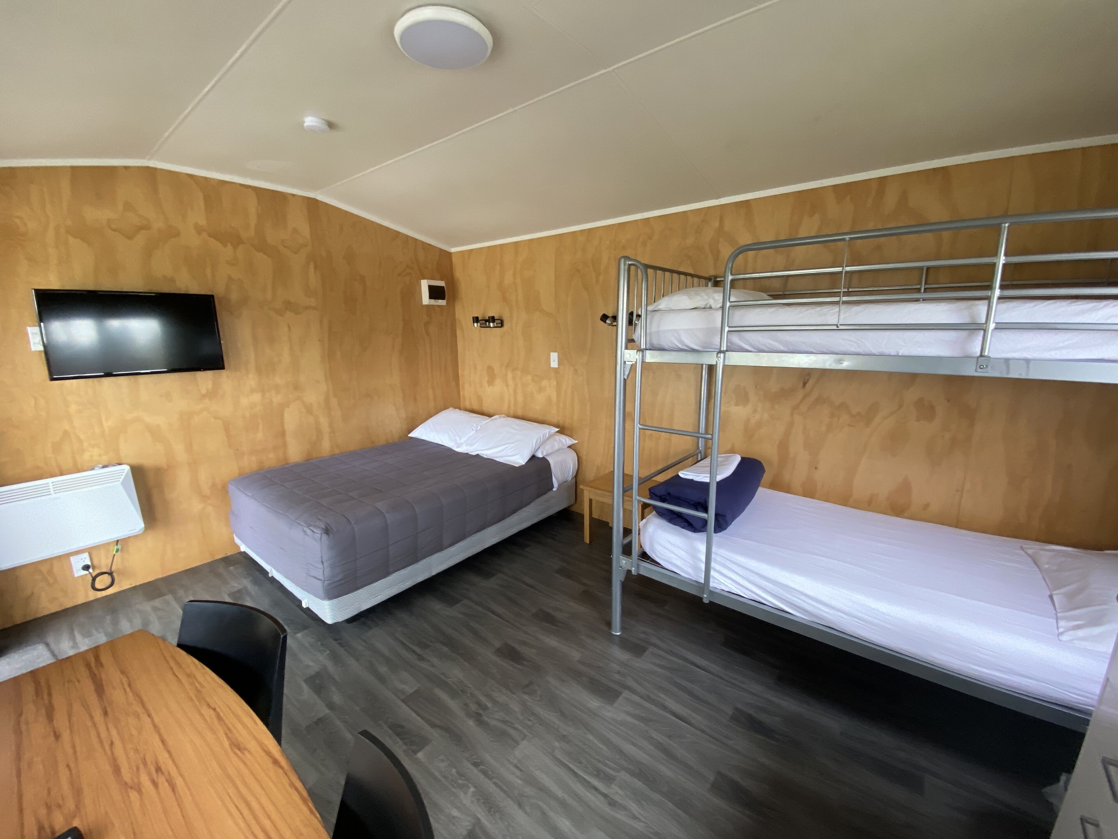 Une chambre avec deux lits simples, un lit superposé, un bureau, une chaise, une télévision et un radiateur.
