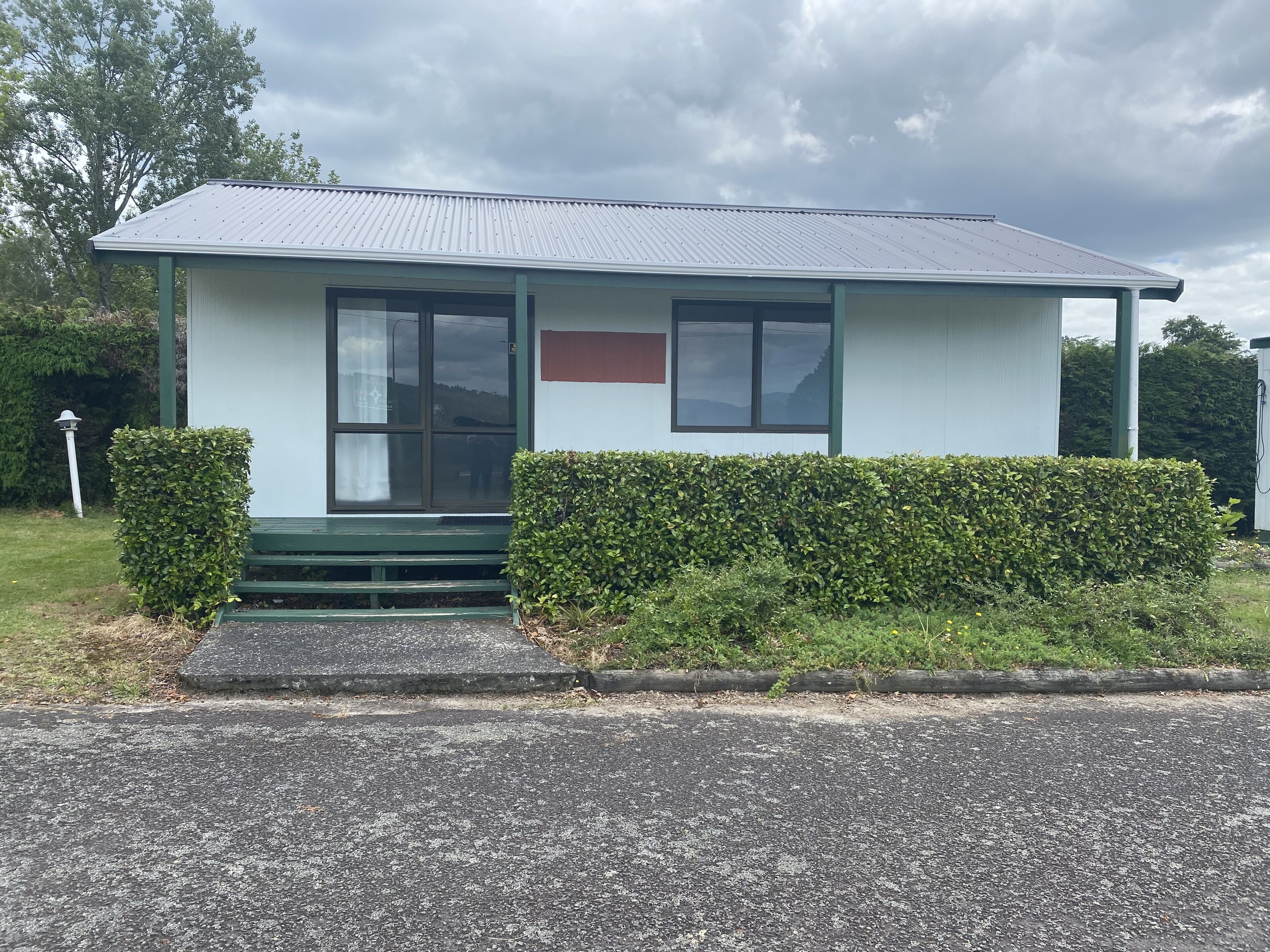 A small, single-story building with a metal roof and a green bench outside.