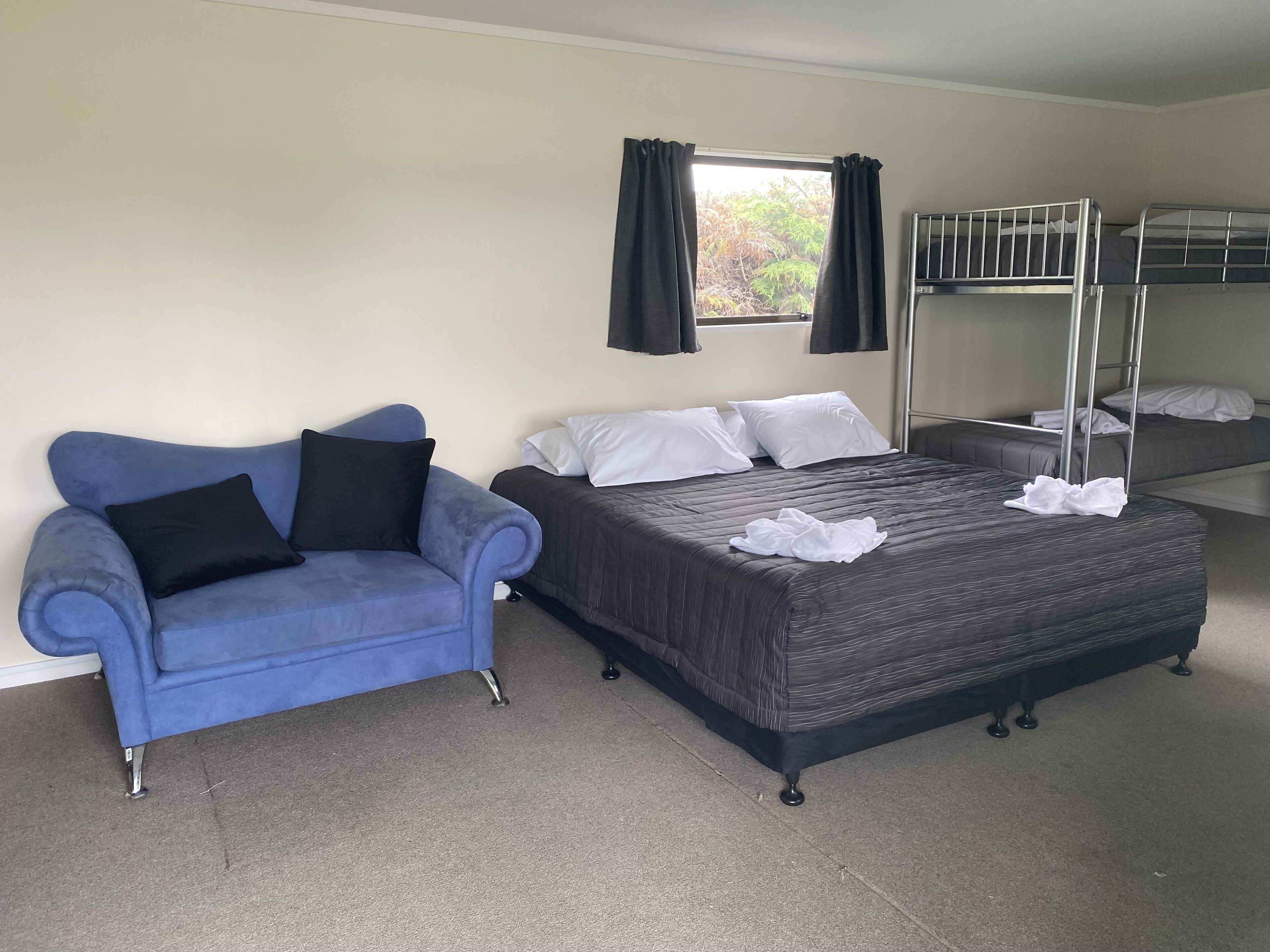 Una stanza con un letto a castello, un divano blu con cuscini neri e una finestra con tende.