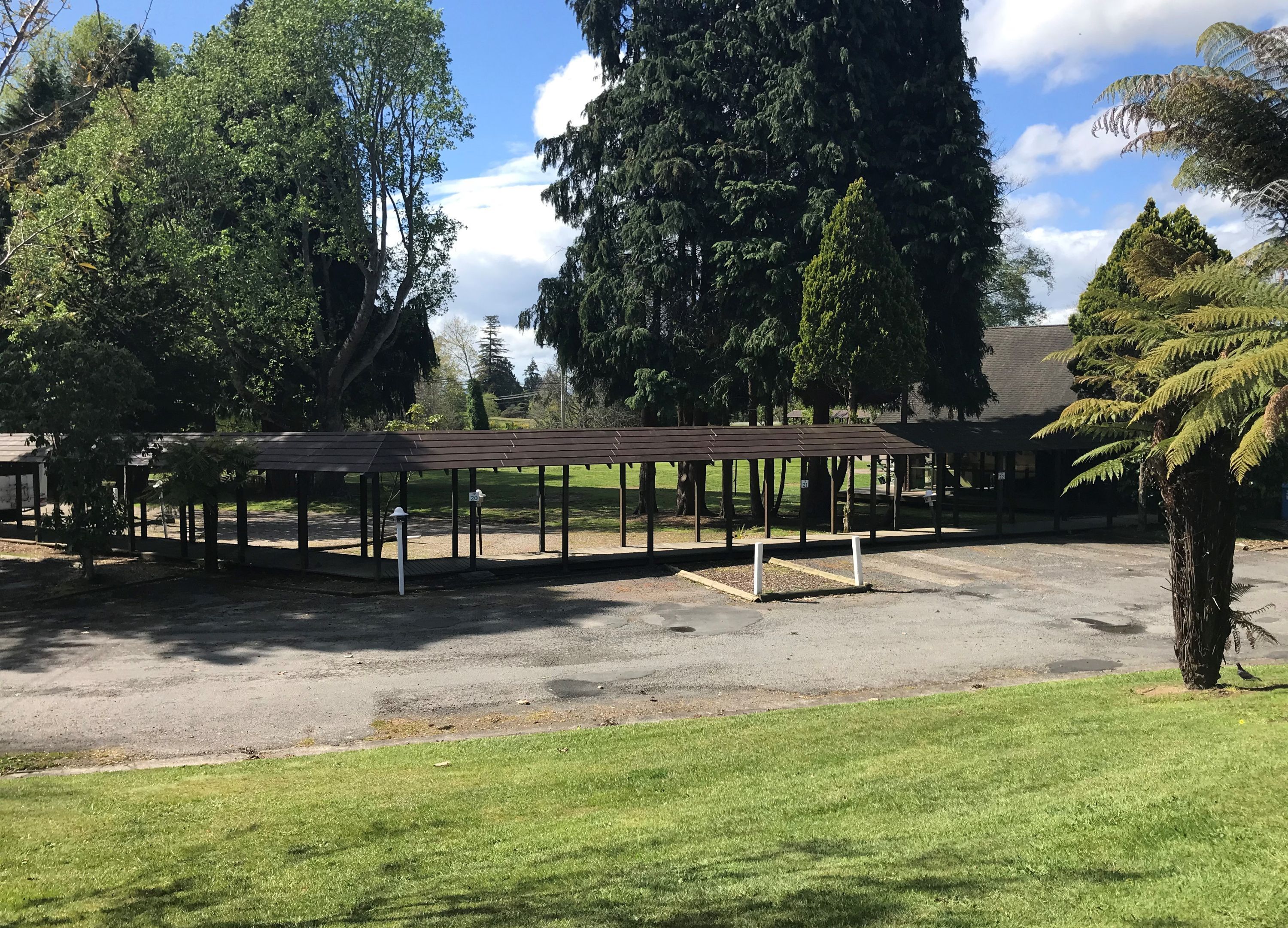 A covered pavilion with a gravel ground, surrounded by trees and grass.
