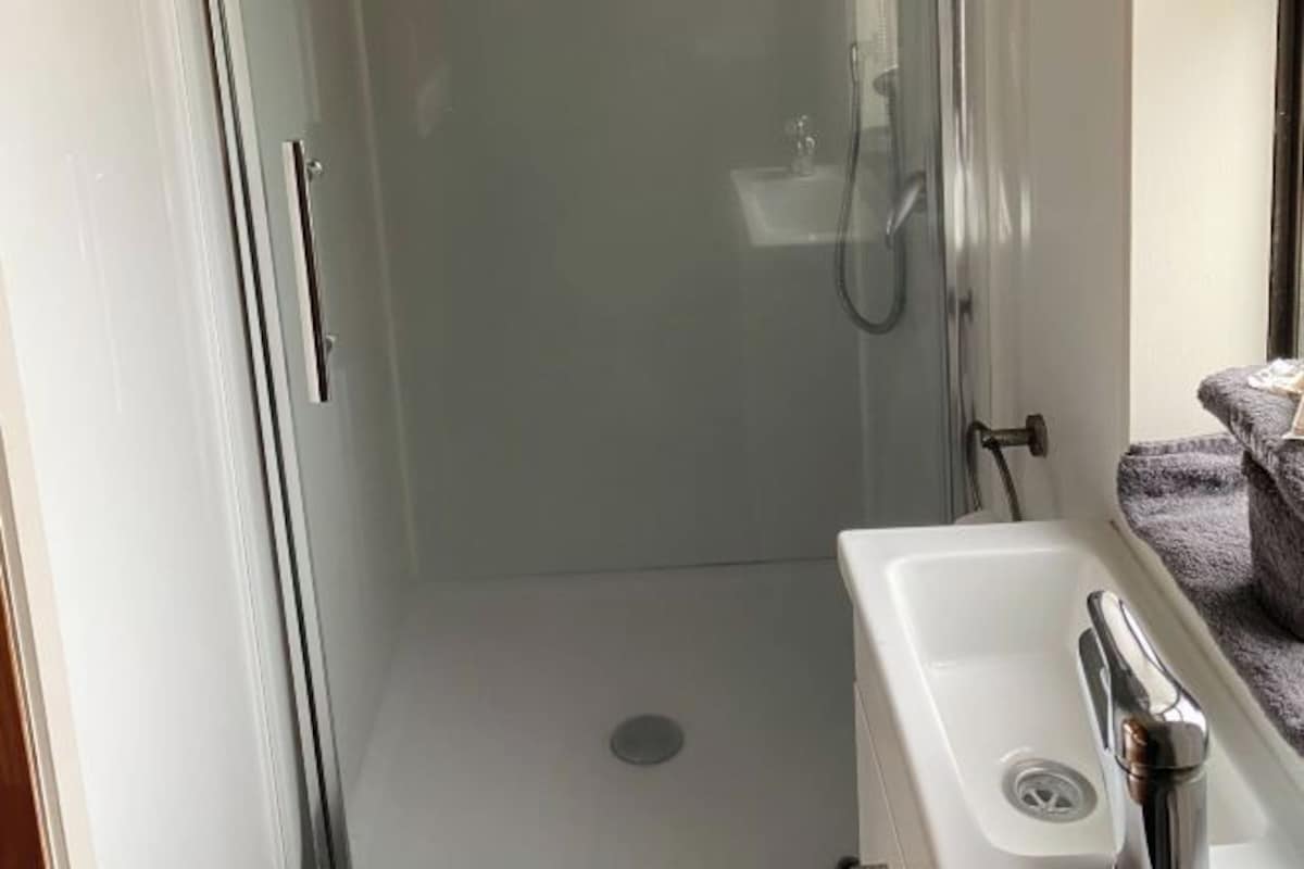 Une salle de bain avec une douche à parois de verre, un lavabo blanc avec un robinet chromé et une petite fenêtre.