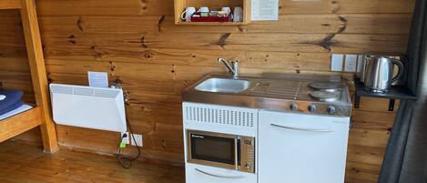 A compact kitchen with a stove, sink, and a small shelf with kitchen items.