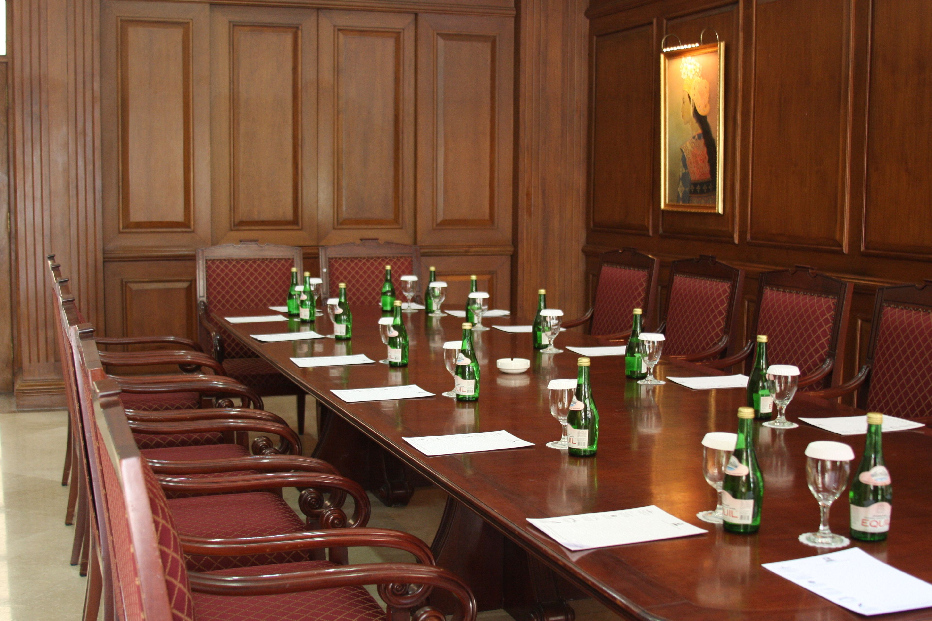 A conference room with a long wooden table, red upholstered chairs, and green bottles of water and wine.