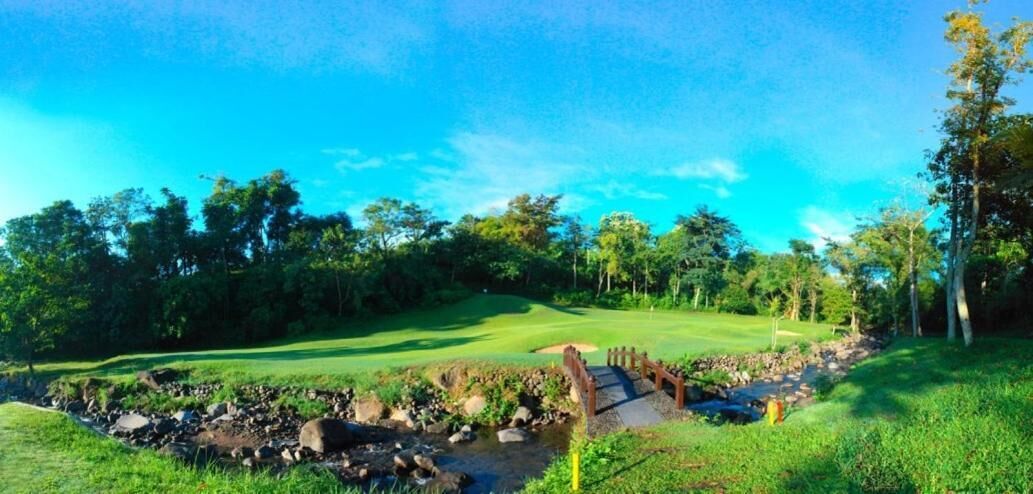 A golf course with a bridge over a stream, surrounded by trees and a clear sky.
