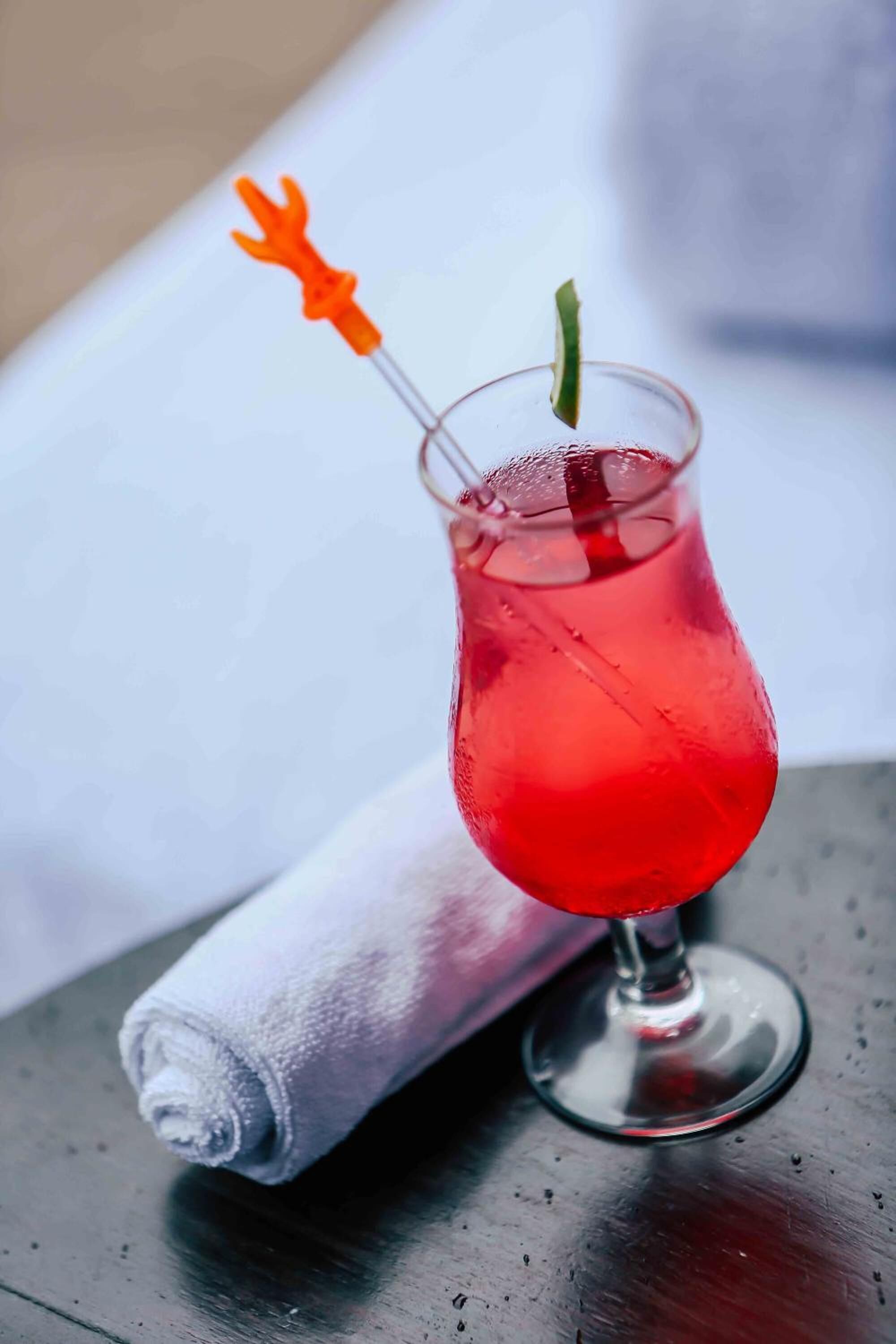 Un verre à cocktail contenant une boisson rouge, une tranche de citron vert et une tranche d’orange, posé sur une table.