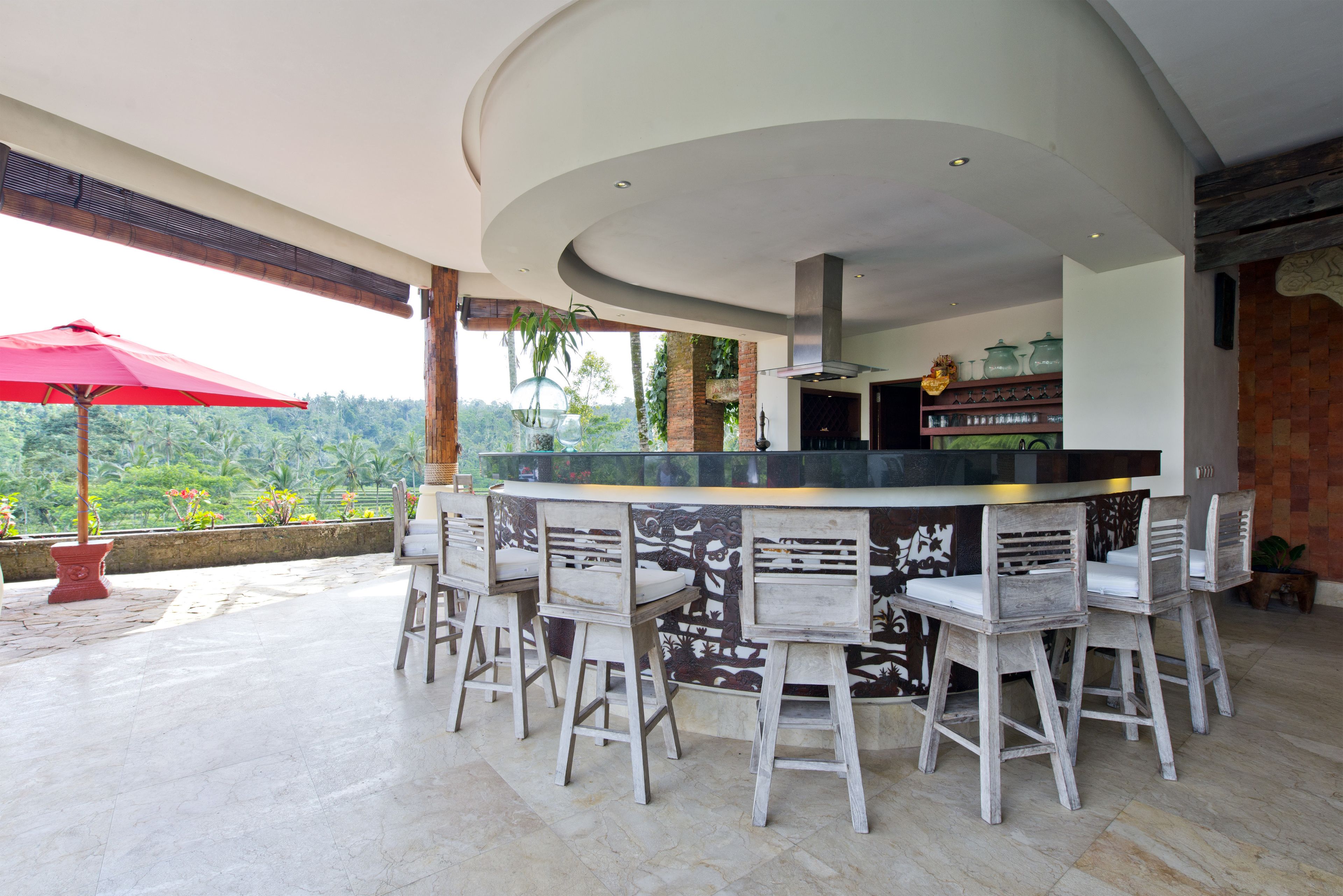 A bar area with a curved ceiling, wooden chairs, and a red umbrella.