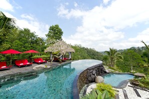 A clear pool with lounge chairs and umbrellas, surrounded by lush greenery and a thatched-roof structure. - Adiwana Dara Ayu (Payangan)