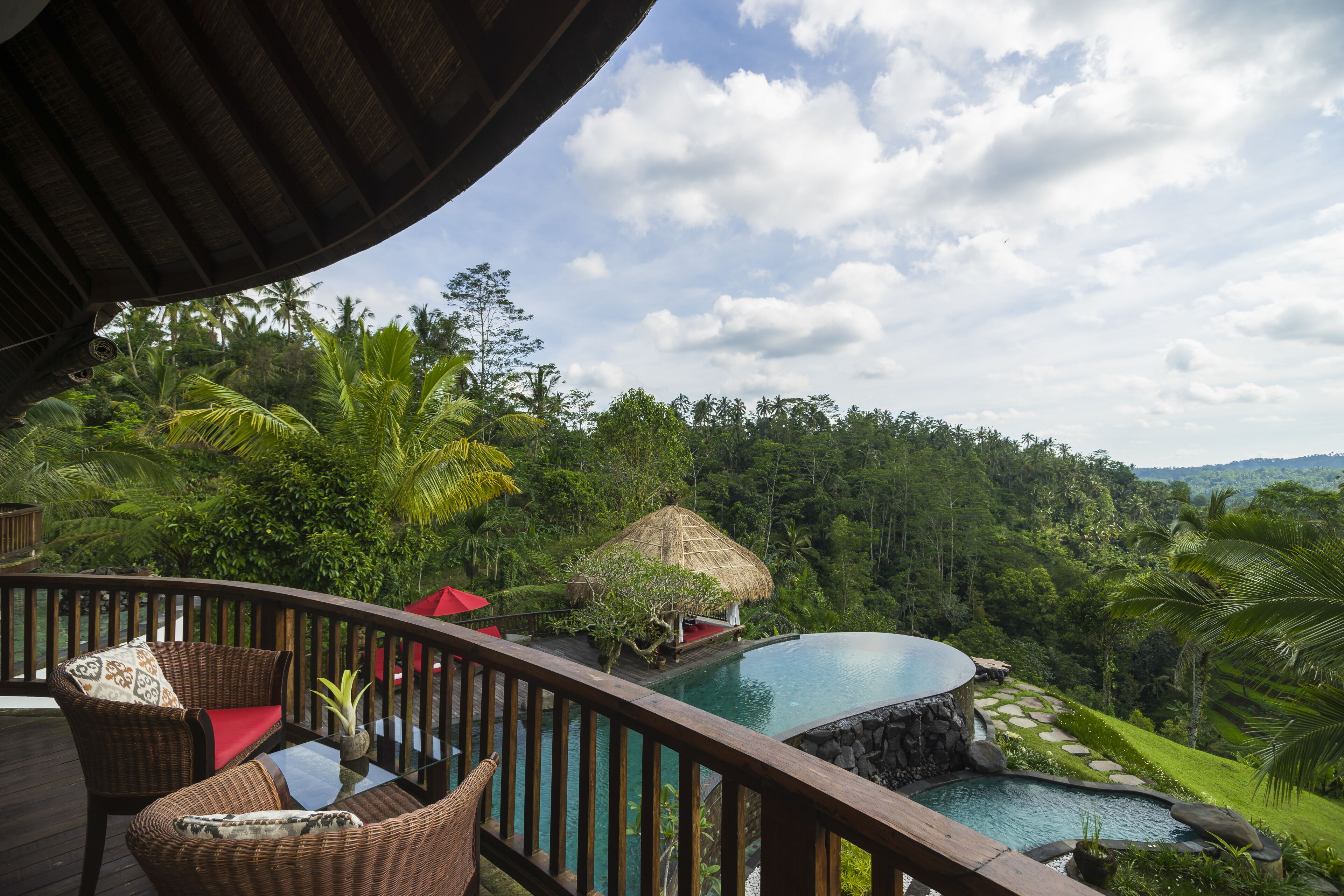 A wooden deck with wicker furniture overlooking a pool and lush greenery.