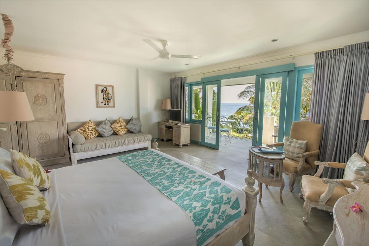 A spacious bedroom with a large bed, a sofa, a TV, and a balcony with a view of the sea.