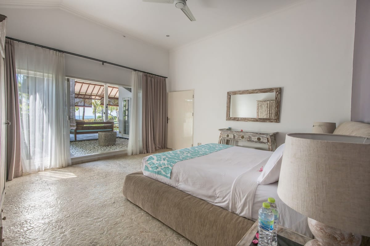 A bedroom with a bed, a nightstand, a lamp, and a view of the outdoors.