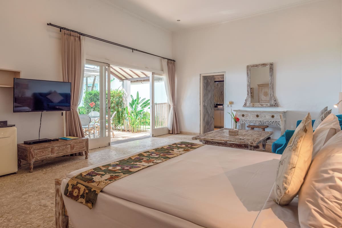 A spacious bedroom with a large bed, a television, a wooden dresser, a fireplace, and a view of the outdoors through a sliding glass door.