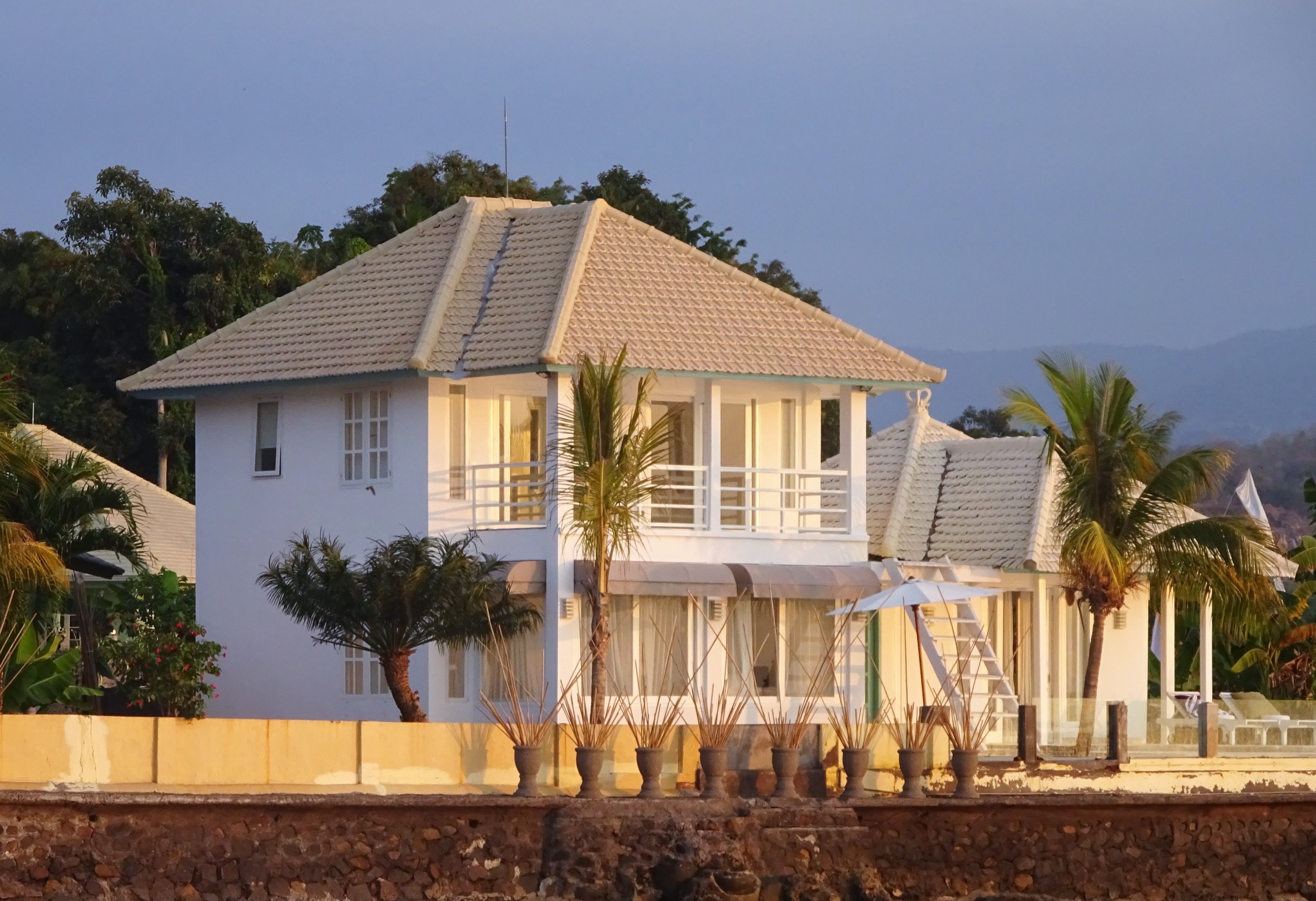 A two-story house with a tiled roof, a balcony, and a staircase leading to a covered area.