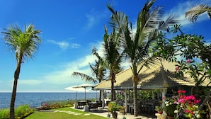 Un resort costero con un porche cubierto, palmeras y vista al mar.