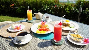 A table set with breakfast items, including fruit, a drink, and a teapot, overlooking a beach.