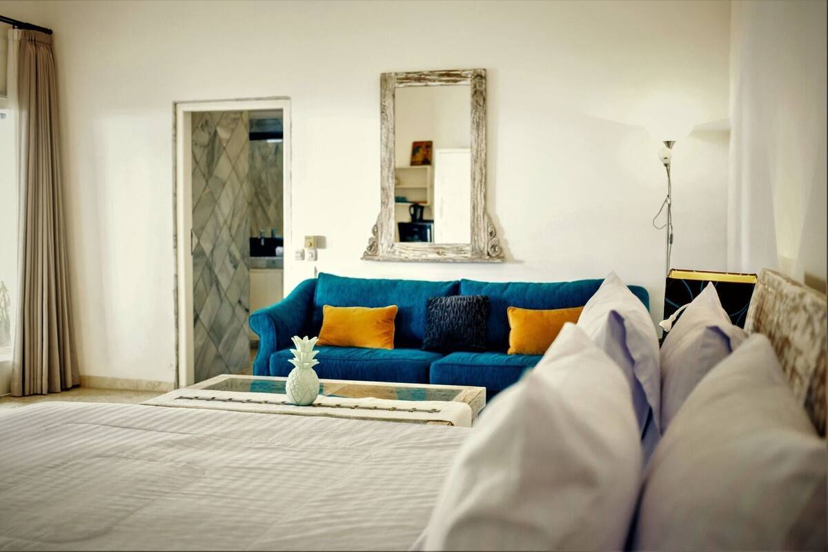 A bedroom with a bed, a blue sofa, a mirror, and a lamp.