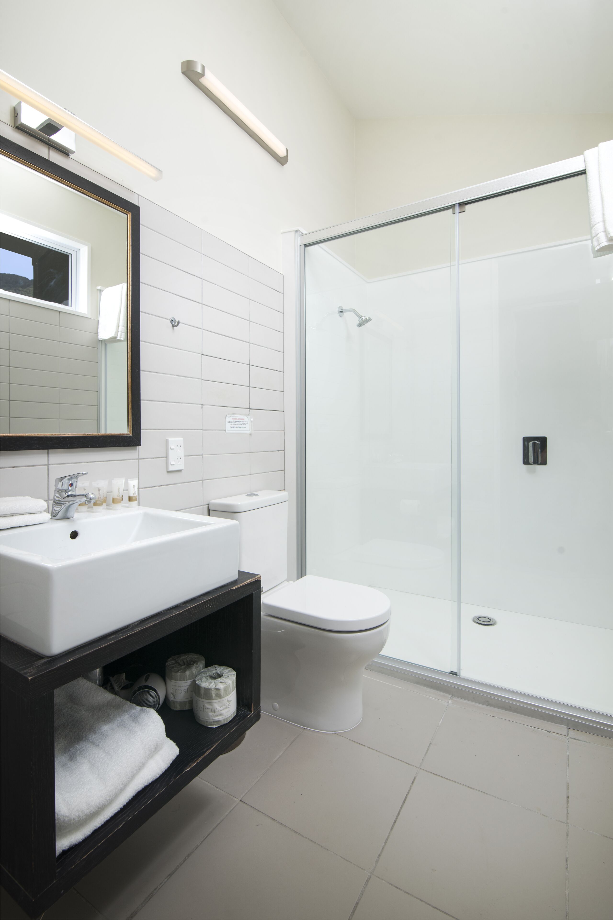 A modern bathroom with a white sink, mirror, and toilet, and a glass-enclosed shower area.