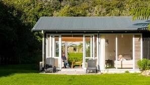A modern house with a covered porch, large windows, and a view of a lush green landscape. - Furneaux Lodge (Endeavour Inlet)