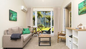 A living room with a beige sofa, a coffee table, a dining table with chairs, and a view of a tropical landscape through a glass door. - Furneaux Lodge (Endeavour Inlet)