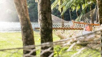 A hammock tied between trees in a grassy area with a body of water in the background.