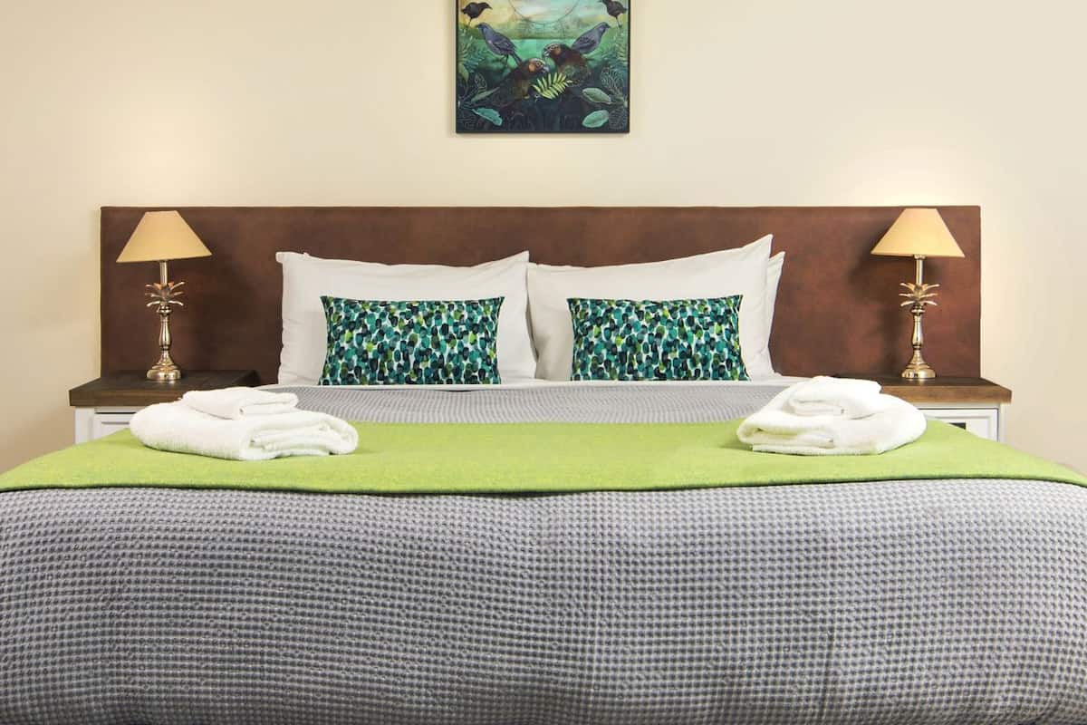 A hotel room with a large bed, two bedside lamps, a green throw blanket, and a painting on the wall.