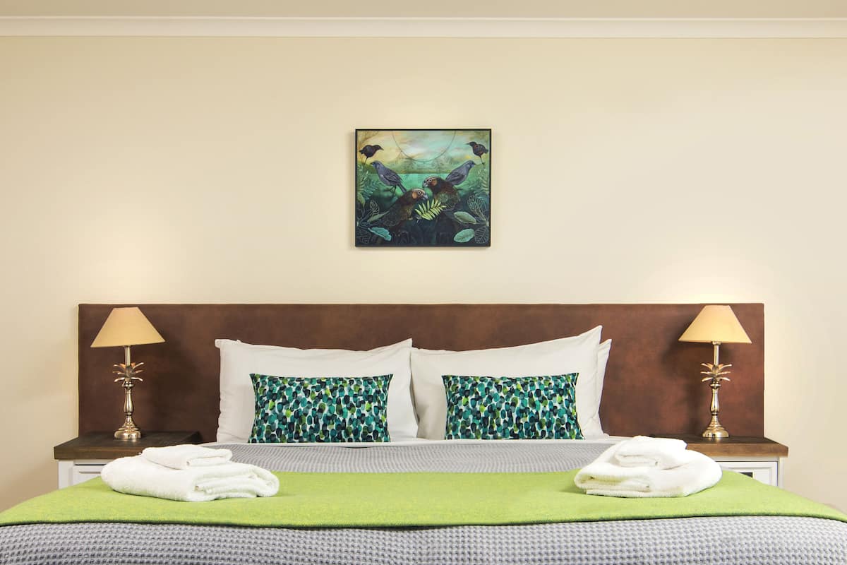 A hotel room with a large bed, two pillows, two bedside lamps, and a painting on the wall.