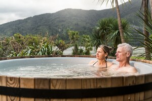 Uma banheira de hidromassagem com estrutura de madeira, rodeada por vegetação exuberante e montanhas ao fundo.