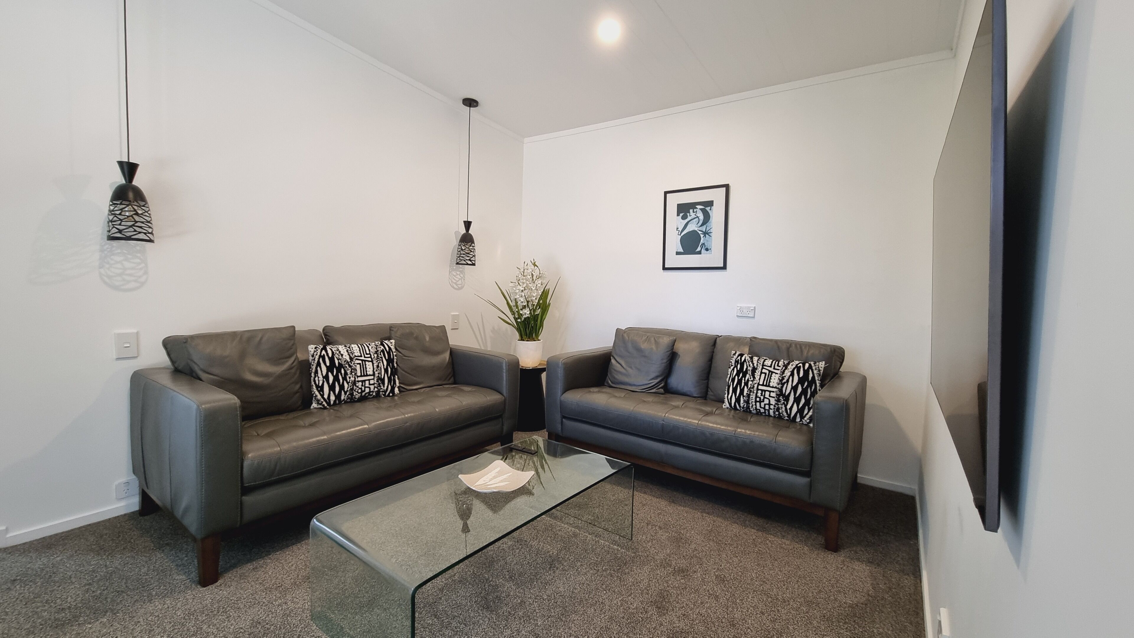 A modern living room with two leather sofas, a glass coffee table, and decorative pillows.