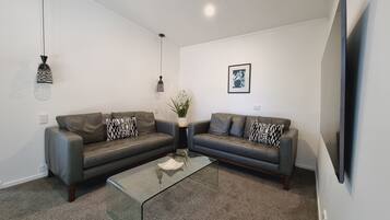 A modern living room with two leather sofas, a glass coffee table, and decorative pillows.