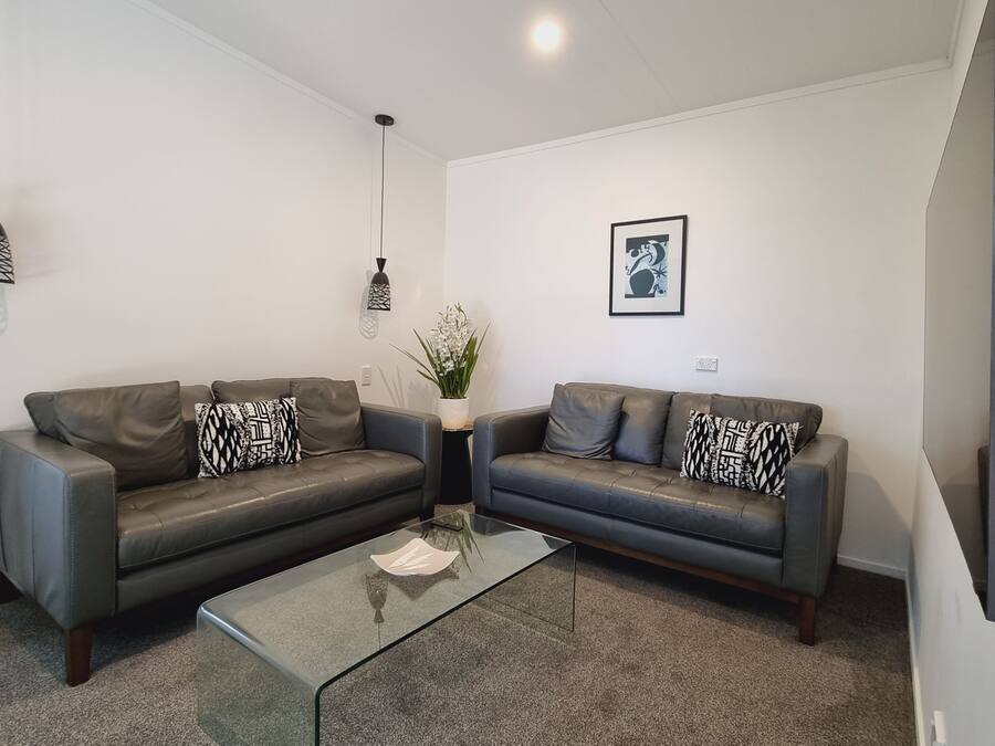 A modern living room with two leather sofas, a glass coffee table, and decorative pillows.