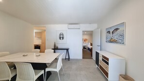 Una habitación moderna y bien iluminada con una mesa de comedor, sillas blancas, una pequeña área de cocina y un cuadro en la pared.
