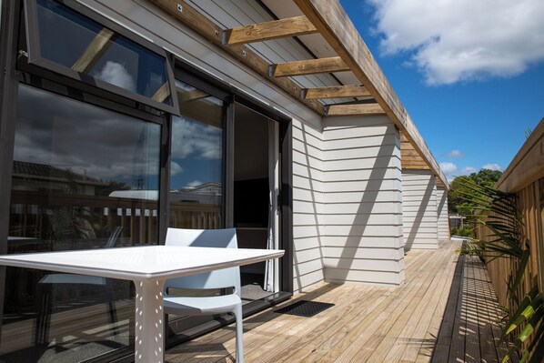 A modern outdoor patio with a table and chairs, large sliding glass doors, and wooden beams. - Peninsula Motel (Whitianga)