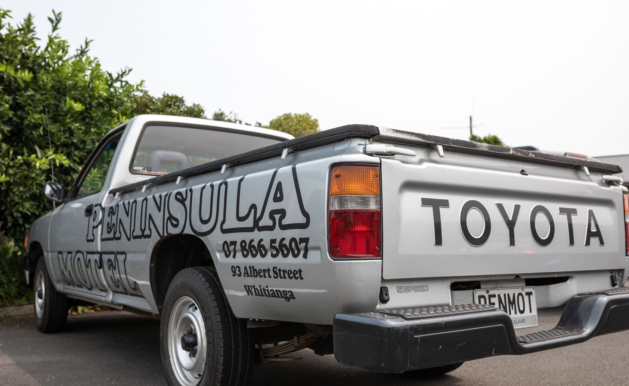 A silver Toyota pickup truck with "PENINSULULA" and a phone number on the side.