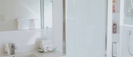 Un baño moderno con ducha de vidrio, un lavamanos blanco con espejo y suelo de madera.