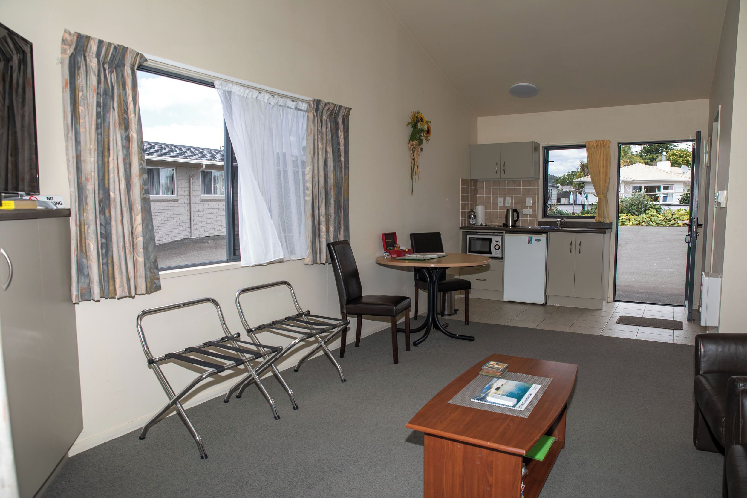 Un espacio habitable compacto con kitchenette, comedor y zona de estar con mesa y sillas.