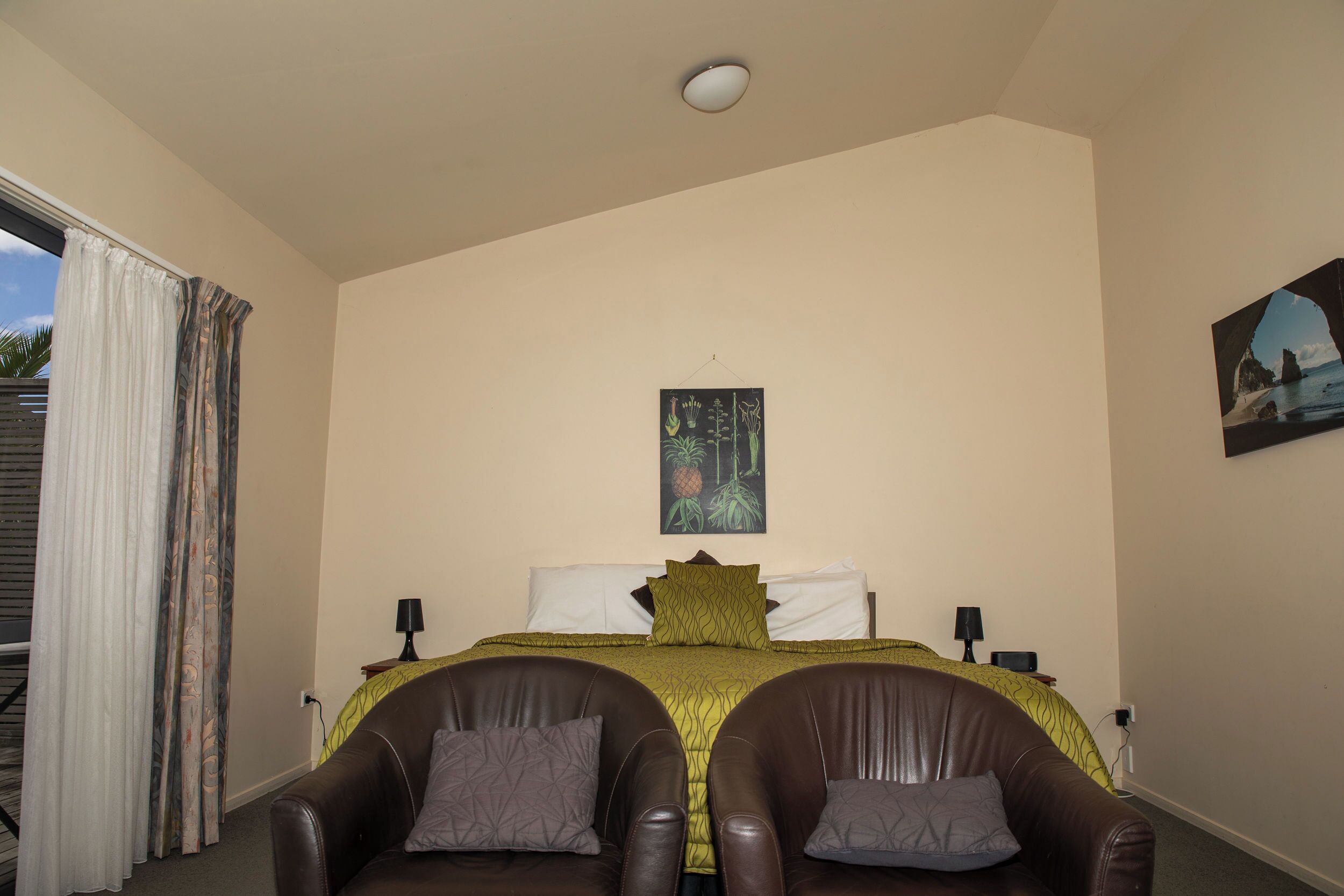 Un dormitorio con una cama, dos sillones de cuero, un cuadro y una ventana con cortinas.