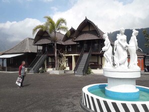 A traditional building with a thatched roof, a staircase, and a statue in front. - Batur Lakeside Huts (Kintamani)