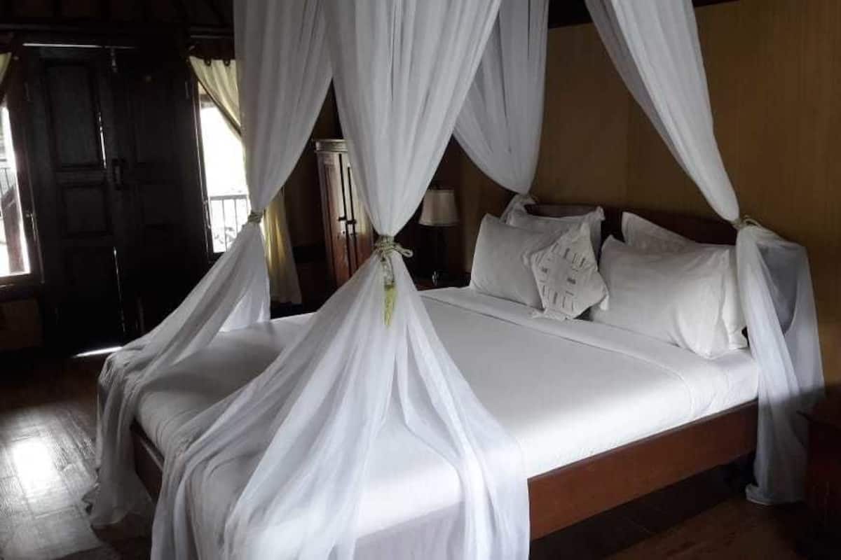 A bed with white bedding and a canopy, a bedside table with a lamp, and a wooden floor.