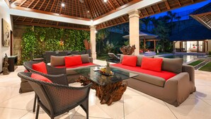 A spacious outdoor lounge area with a glass coffee table, wicker chairs, and a sofa with red cushions.