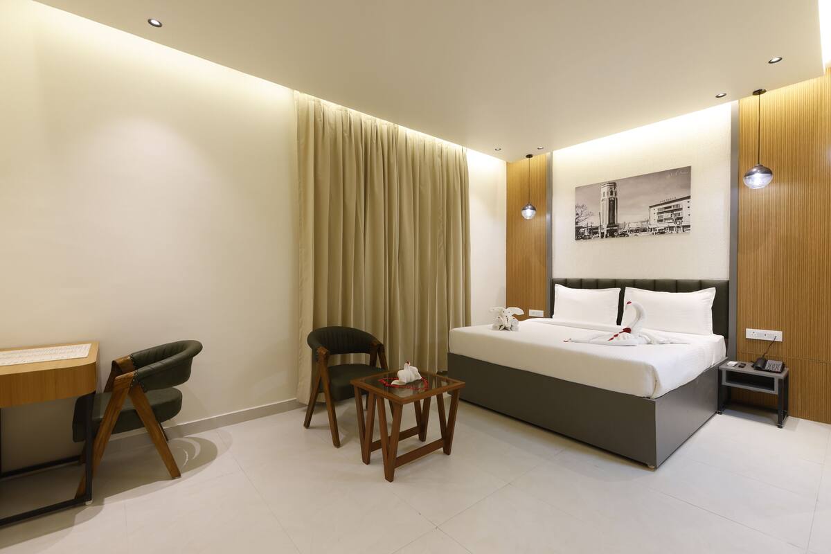 A modern hotel room with a bed, a desk, a chair, a small table, and a nightstand.