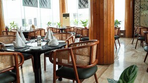 Un restaurante con mobiliario de madera, ventanas amplias y plantas en macetas.