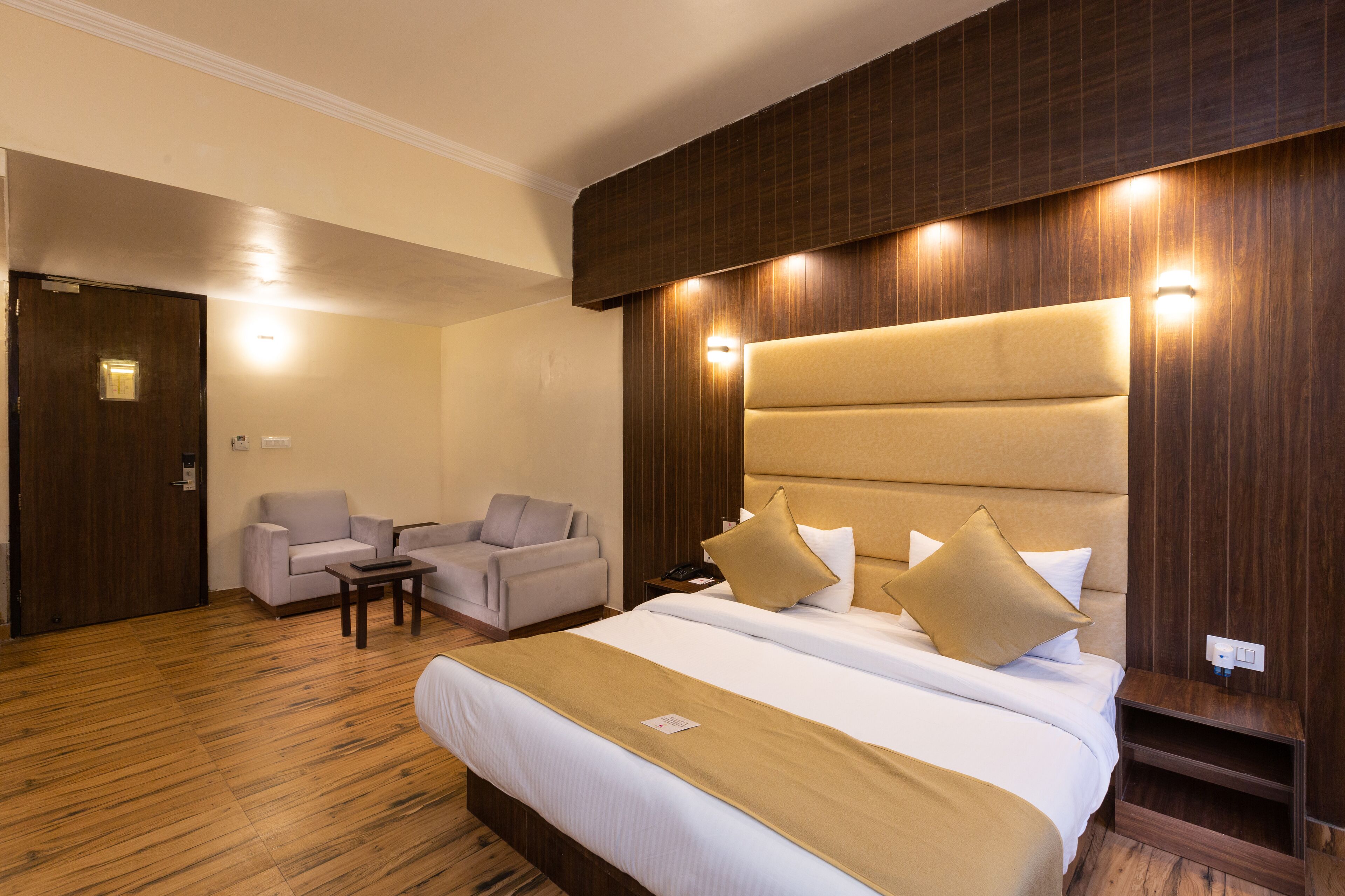A hotel room with a large bed, a sofa, a small table, and a wooden headboard.