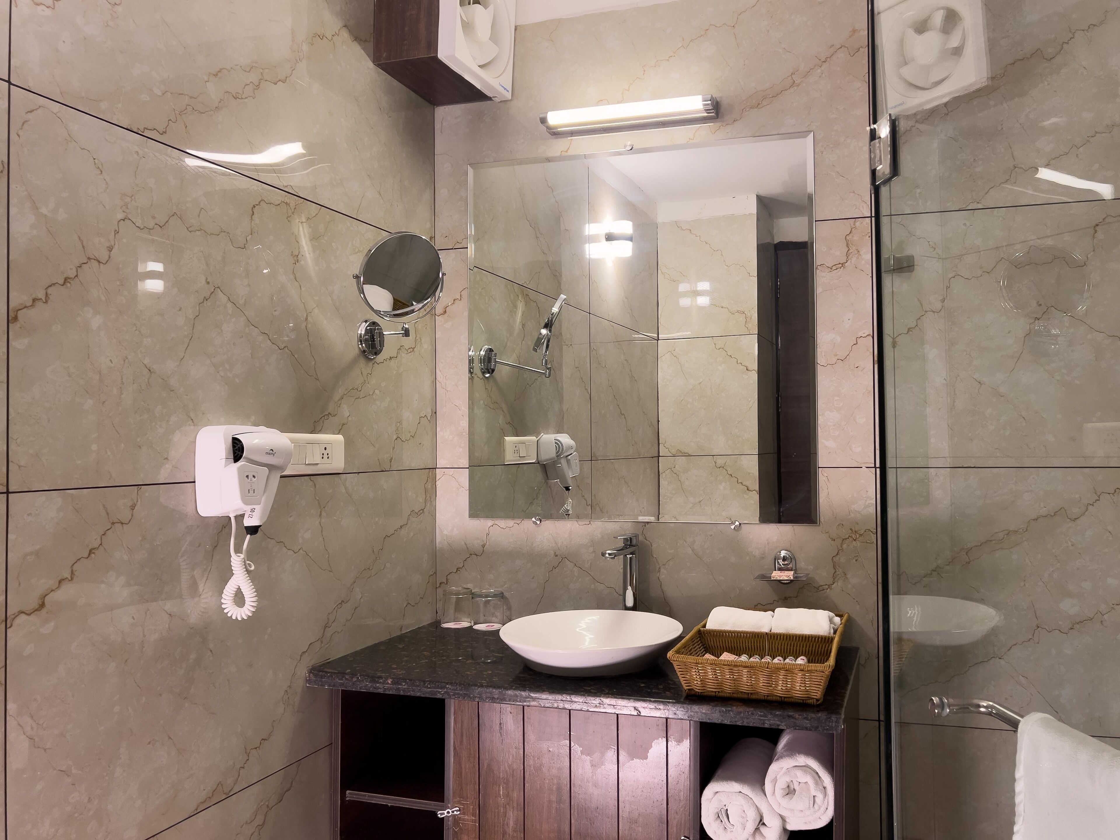 A modern bathroom with a marble floor, a round mirror, a white sink, a hairdryer, and a towel rack.