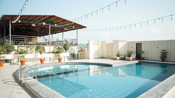 Una piscina en la azotea con una zona de estar cubierta, plantas en macetas y luces colgantes.