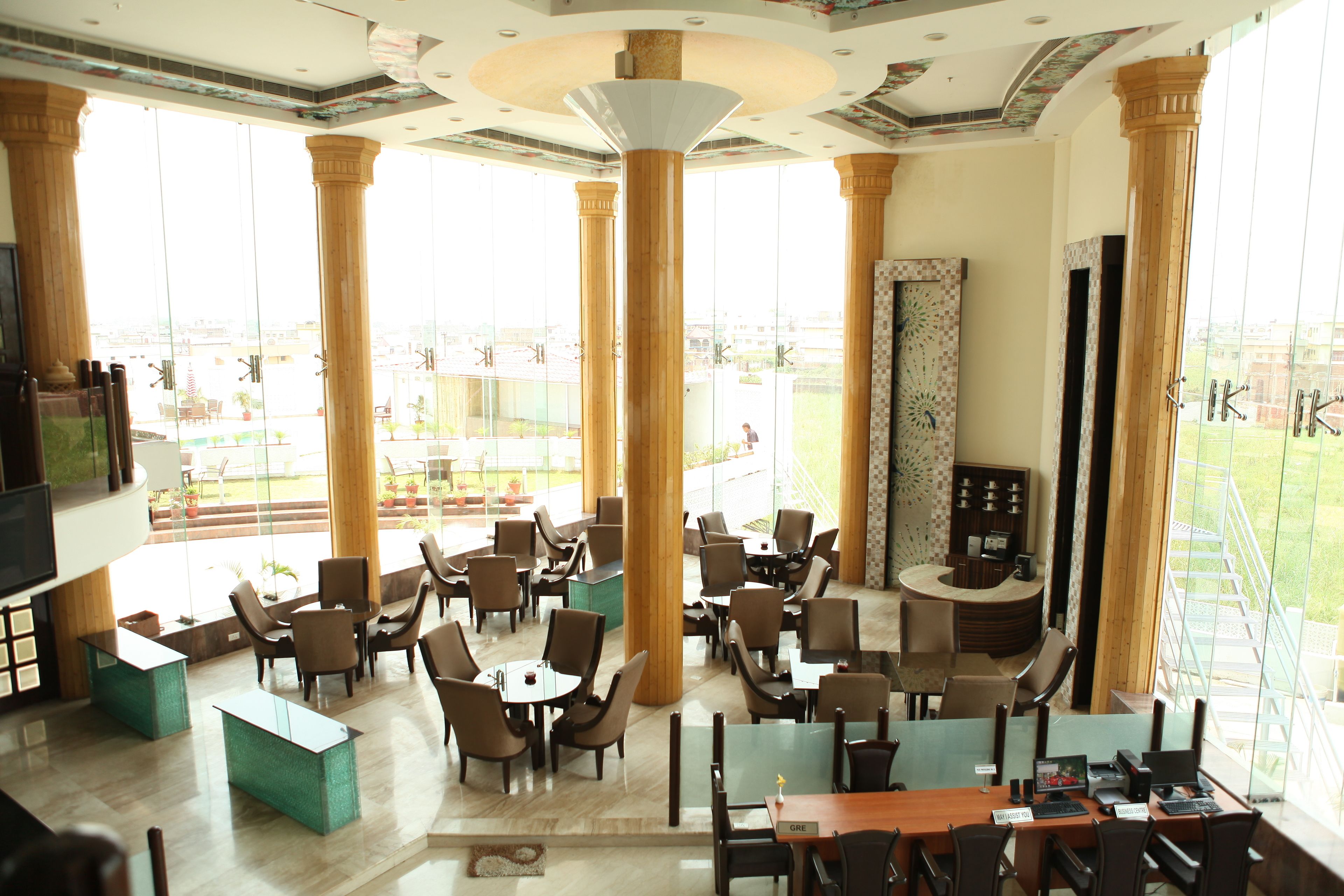 A spacious hotel lobby with high ceilings, large windows, and a central seating area with tables and chairs.