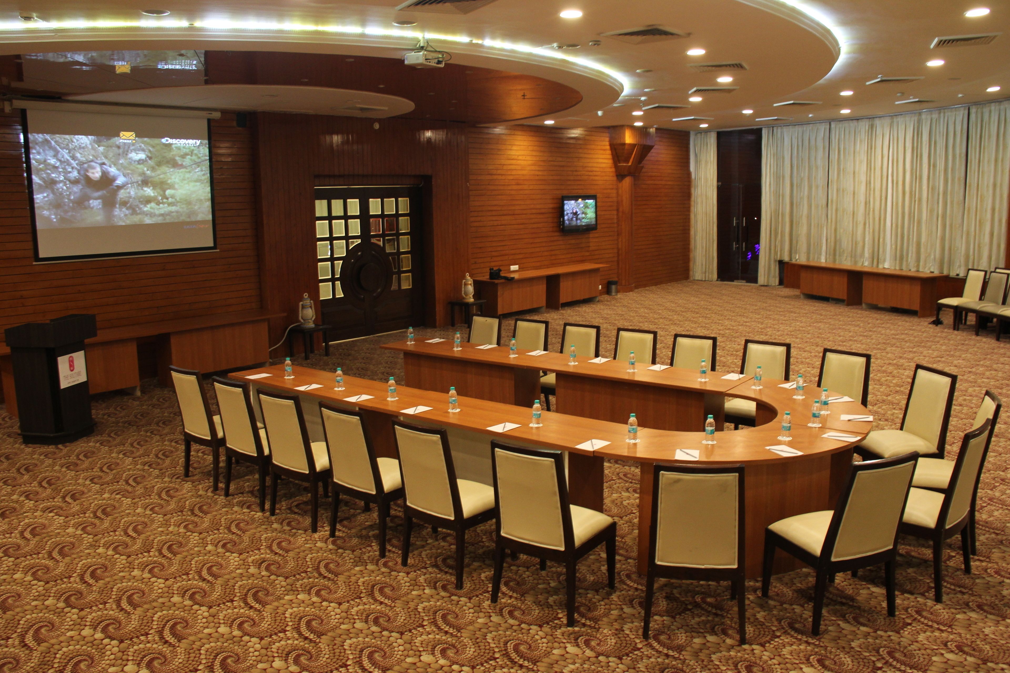 A conference room with a long table, chairs, a podium, a screen, and a large window.