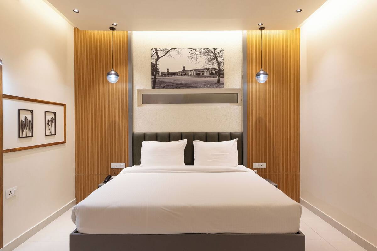 A modern bedroom with a large bed, wooden paneling, two pendant lights, and a framed picture on the wall.